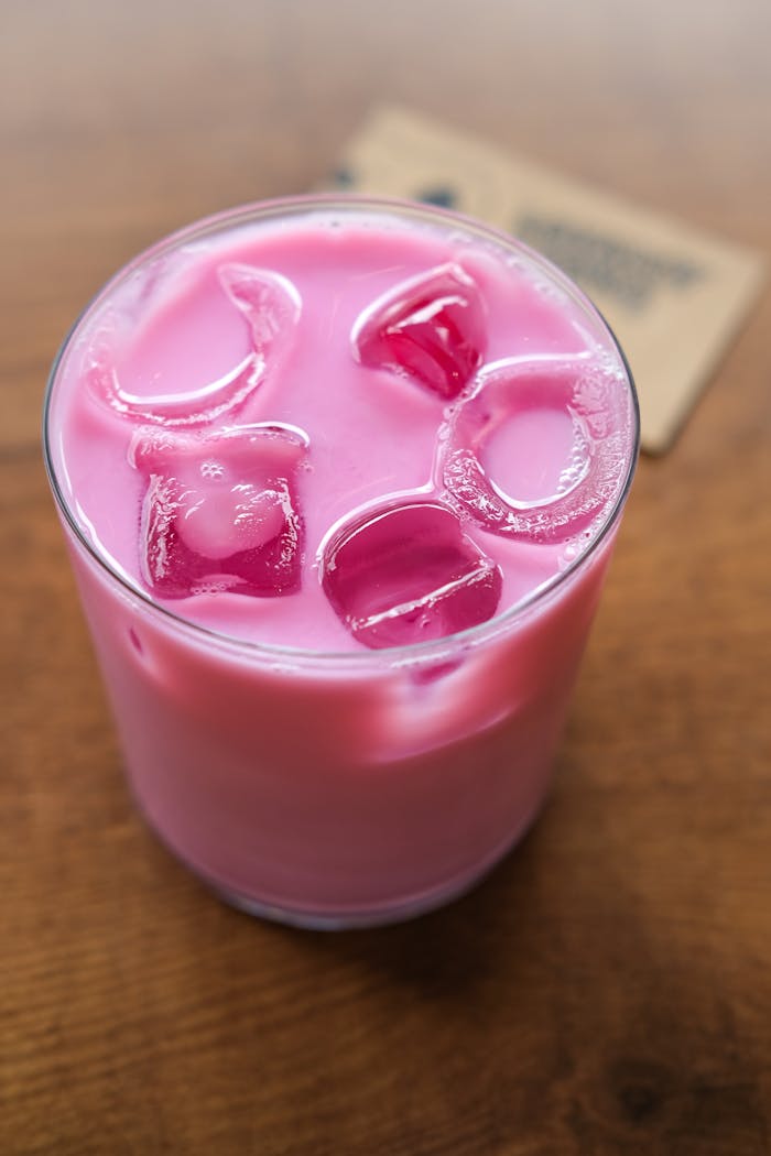 Top-down view of a vibrant pink iced drink with ice cubes, set on a wooden table.