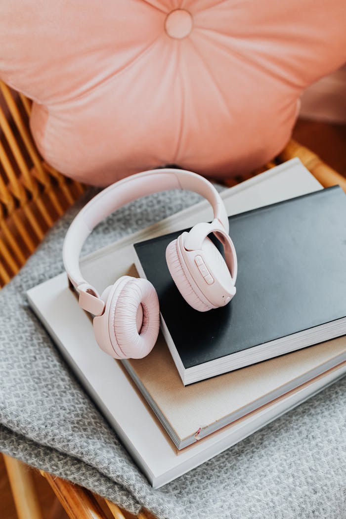Pink wireless headphones resting on a stack of notebooks with a cozy aesthetic.
